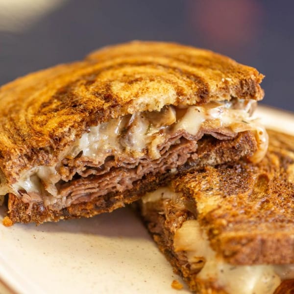 Close-up of a grilled sandwich, cut in half, revealing melted cheese and thinly sliced meat.